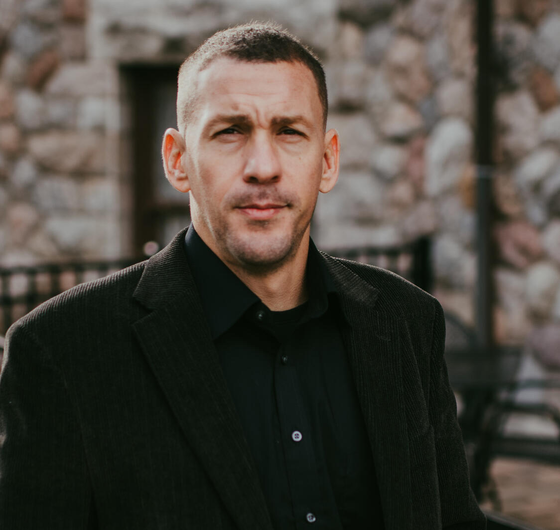 Professional headshot of Alex Van Galder, lead commercial muralist and founder of VanGalder Murals, dressed professionally in a suit jacket outside a stone architectural building